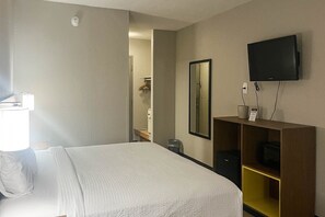 Habitación de hotel con cama, televisor montado en la pared, escritorio pequeño con silla y espejo.
