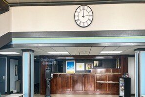 Un área de recepción con un reloj, un quiosco de registro y una zona de bar.