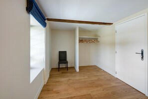 A hallway with a wooden floor, a black chair, a white door, and a coat rack with hangers. - Holiday Home 'La Colonie - Grange Arthuis' with Private Terrace, Wi-Fi and Air Conditioning (Lavau)