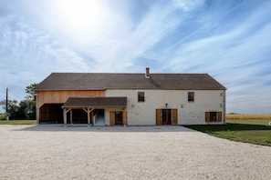 A two-story building with a gravel driveway, wooden doors, and a covered porch. - Holiday Home 'La Colonie - Grange Arthuis' with Private Terrace, Wi-Fi and Air Conditioning (Lavau)