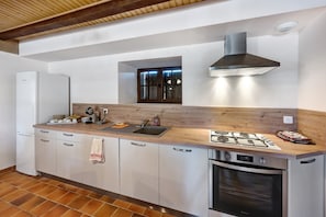A kitchen with a built-in oven, a stove, a sink, and a window above the countertop. - Holiday Home 'La Colonie - Grange Arthuis' with Private Terrace, Wi-Fi and Air Conditioning (Lavau)