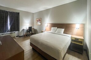Une chambre d’hôtel avec un grand lit, un bureau avec une chaise, une petite table et une table de chevet avec une lampe.