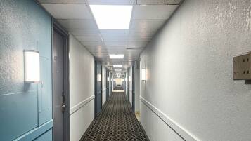 Pasillo de hotel con puertas a ambos lados, alfombra estampada e iluminación empotrada en las paredes.