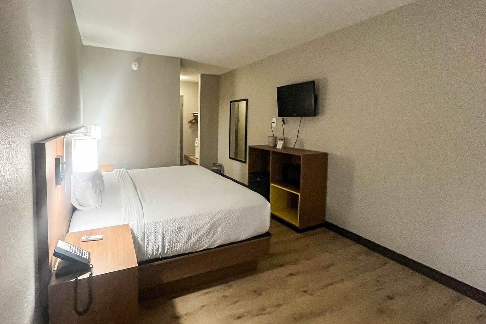 Hotellihuone, jossa on sänky, yöpöytä, lamppu, televisio ja peili.