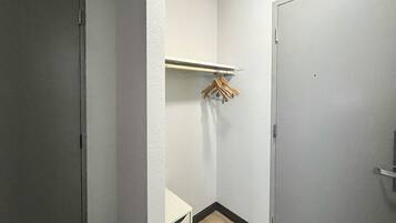 A small, narrow hallway with a white door on the right and a white wall with a wooden hanger rack on the left.
