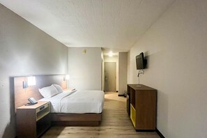 A hotel room with a bed, bedside table with a phone, a desk with a computer, a TV mounted on the wall, and a door leading to another room. - 1 King Bed | Non-Smoking, Micfridge (Fremont (OH))