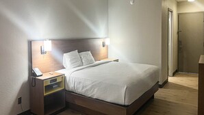 Quarto de hotel com cama, mesas de cabeceira, telefone e luminária na parede.