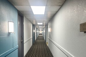 Un long couloir étroit, typique des hôtels, avec des portes des deux côtés, un tapis à motifs et des appliques murales.