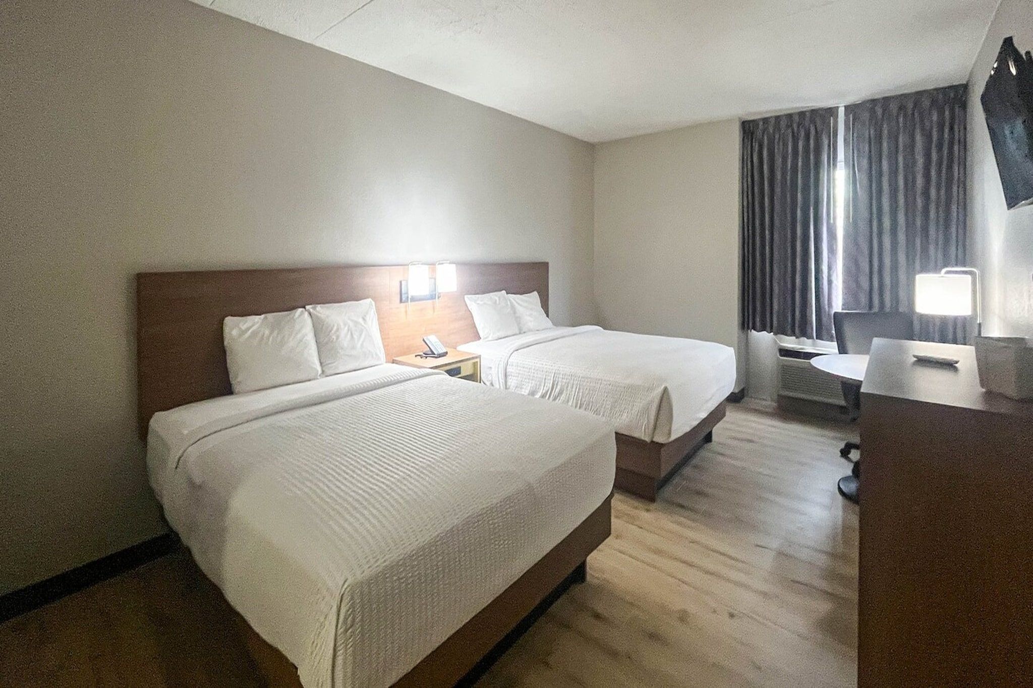 A hotel room with two beds, a desk, a chair, a TV, and a window with curtains.