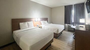 A hotel room with two beds, a desk, a chair, a TV, and a window with curtains.