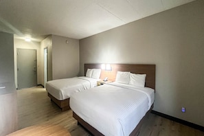 Une chambre d’hôtel avec deux lits, une tête de lit en bois, une table de chevet avec un téléphone et une porte donnant sur une autre pièce.