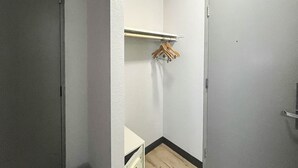 A small, narrow hallway with a white door on the right and a white wall with a wooden hanger rack on the left.