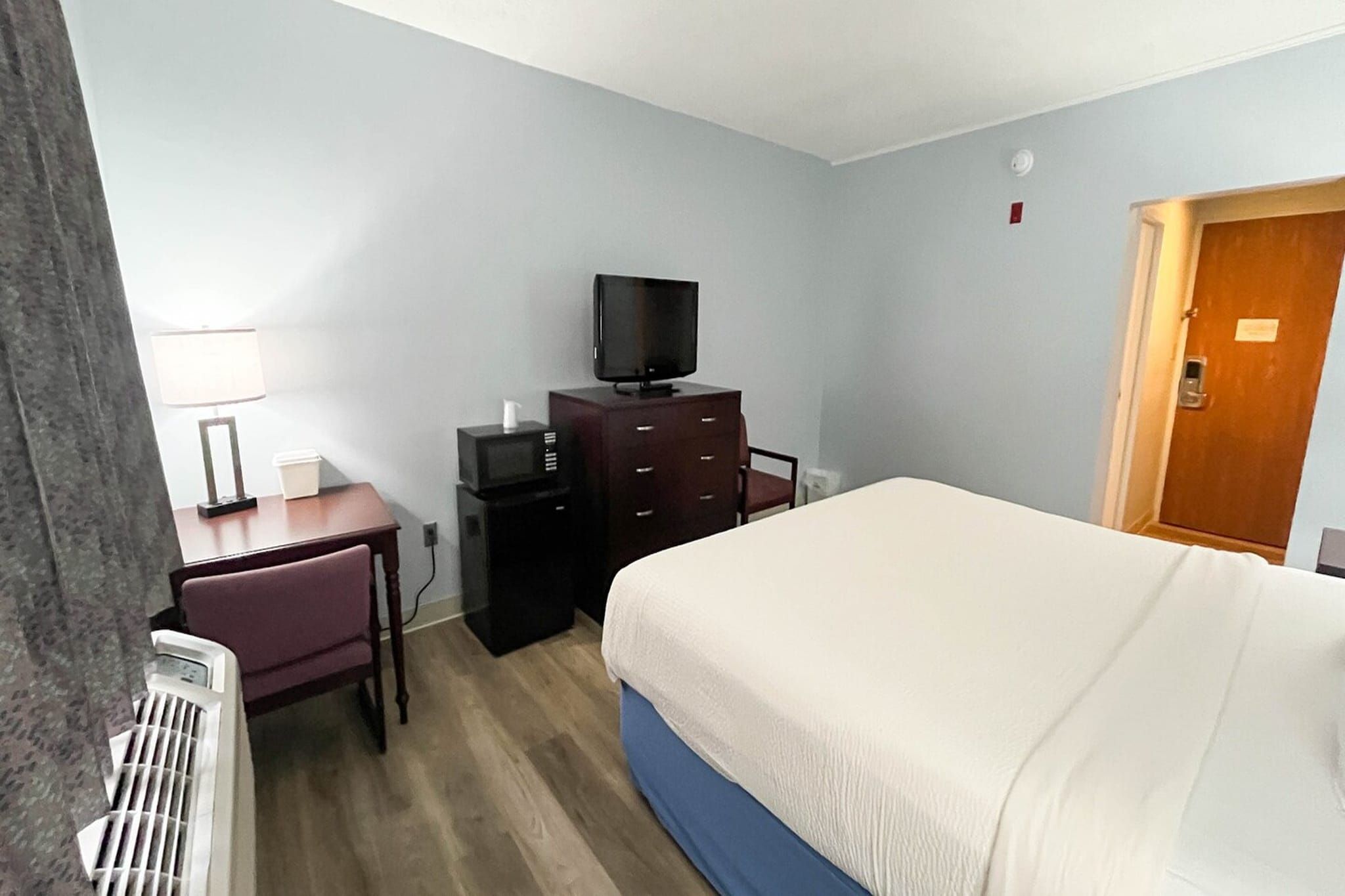 A hotel room with a bed, a desk, a television, and a dresser.