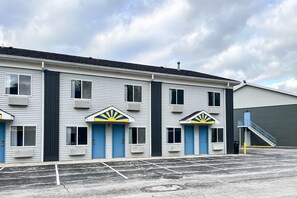 A motel with a row of rooms, each with a blue door and a sun emblem above the door.