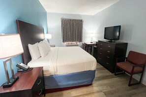 A hotel room with a bed, a desk with a telephone, a television, a chair, and a desk lamp.