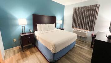 A hotel room with a bed, bedside lamps, a desk, and an air conditioning unit.
