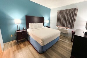 A hotel room with a bed, bedside lamps, a desk, and an air conditioning unit.