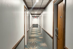 A hotel hallway with a patterned carpet, wooden doors, and a ceiling with recessed lighting.