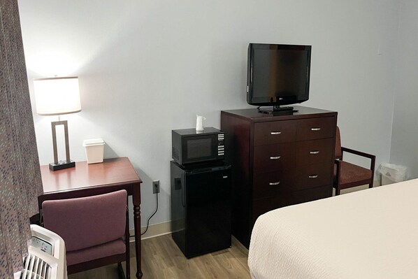 A hotel room with a bed, a desk with a lamp, a television on a dresser, and a microwave.