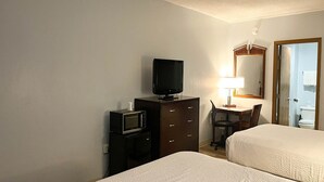 A hotel room with two beds, a television, a desk with a lamp, and a mirror.