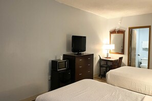 A hotel room with two beds, a television, a desk with a lamp, and a mirror.