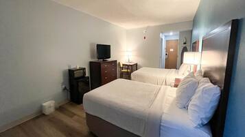 A hotel room with two beds, a television, a desk, and a lamp.