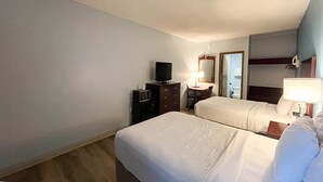A hotel room with two beds, a television, a desk, and a mirror.
