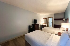 A hotel room with two beds, a television, a desk, and a mirror.