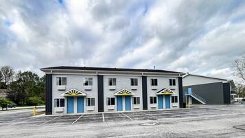 A building with three doors, a parking lot, and a large industrial structure in the background.