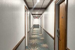 A hotel hallway with a patterned carpet, wooden doors, and a ceiling with recessed lighting.