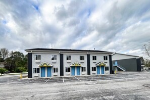 A building with three doors, a parking lot, and a large industrial structure in the background.