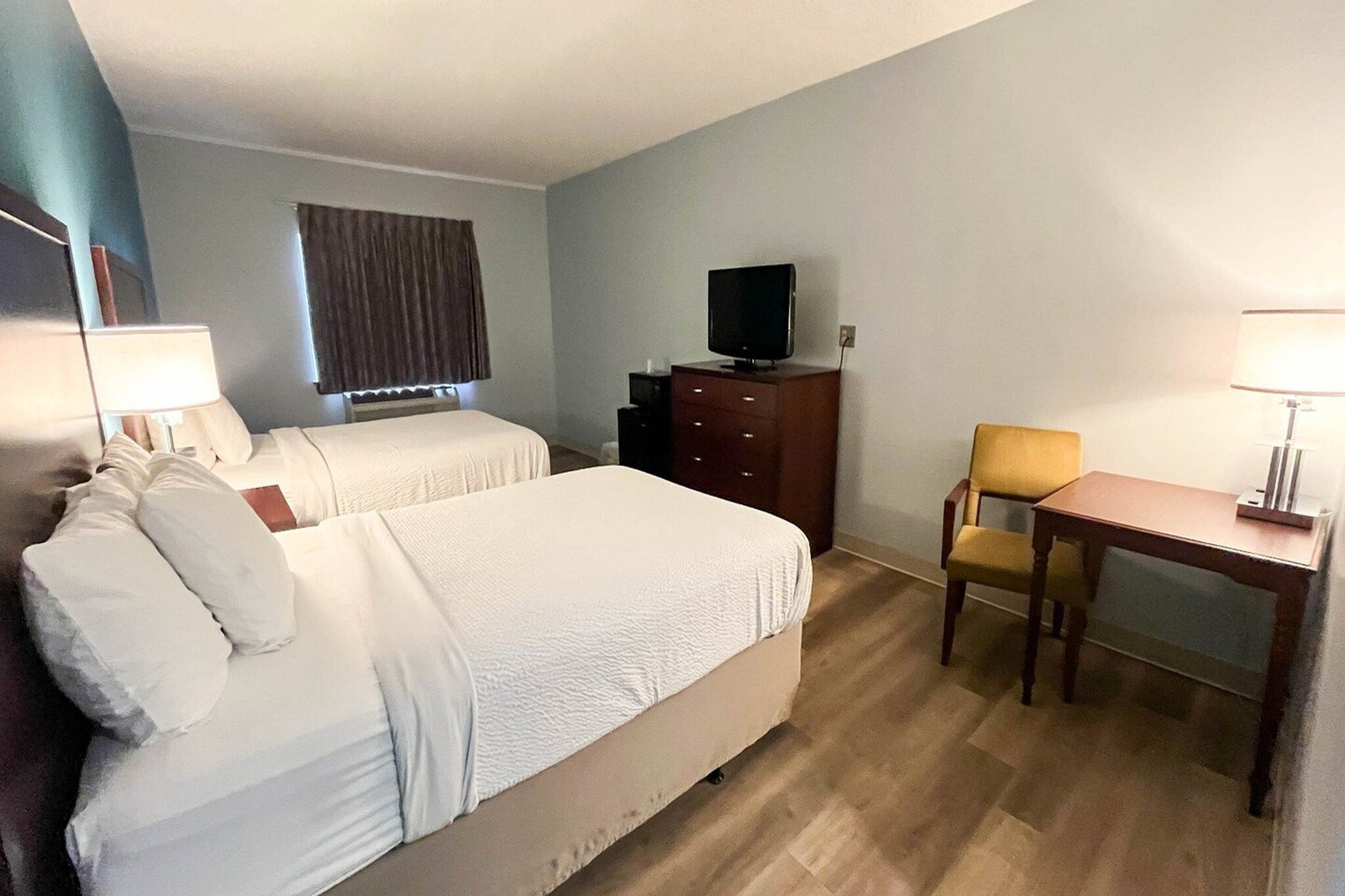 Une chambre d’hôtel avec deux lits, un bureau, une chaise, une télévision et une lampe.