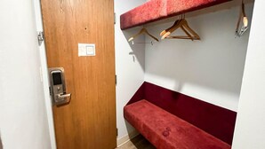 A room with a wooden door, a red bench, and a wall-mounted rack with hangers.