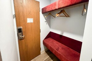 Una habitación con puerta de madera, un banco rojo y un perchero montado en la pared.