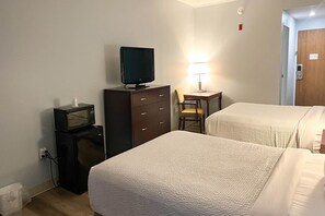 A hotel room with two beds, a desk with a chair, a television on a dresser, and a lamp.