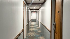 A hotel hallway with a patterned carpet, wooden doors, and a ceiling with recessed lighting.