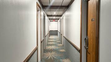 A hotel hallway with a patterned carpet, wooden doors, and a ceiling with recessed lighting.