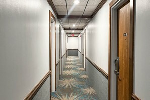 Un pasillo de hotel con alfombra estampada, puertas de madera e iluminación empotrada en el techo.