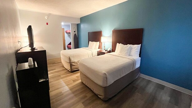 A hotel room with two beds, a desk with a computer, and a view of a hallway.