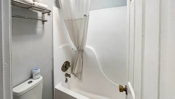 Et lille, lukket badeværelse med badekar, toilet og bruseforhæng.