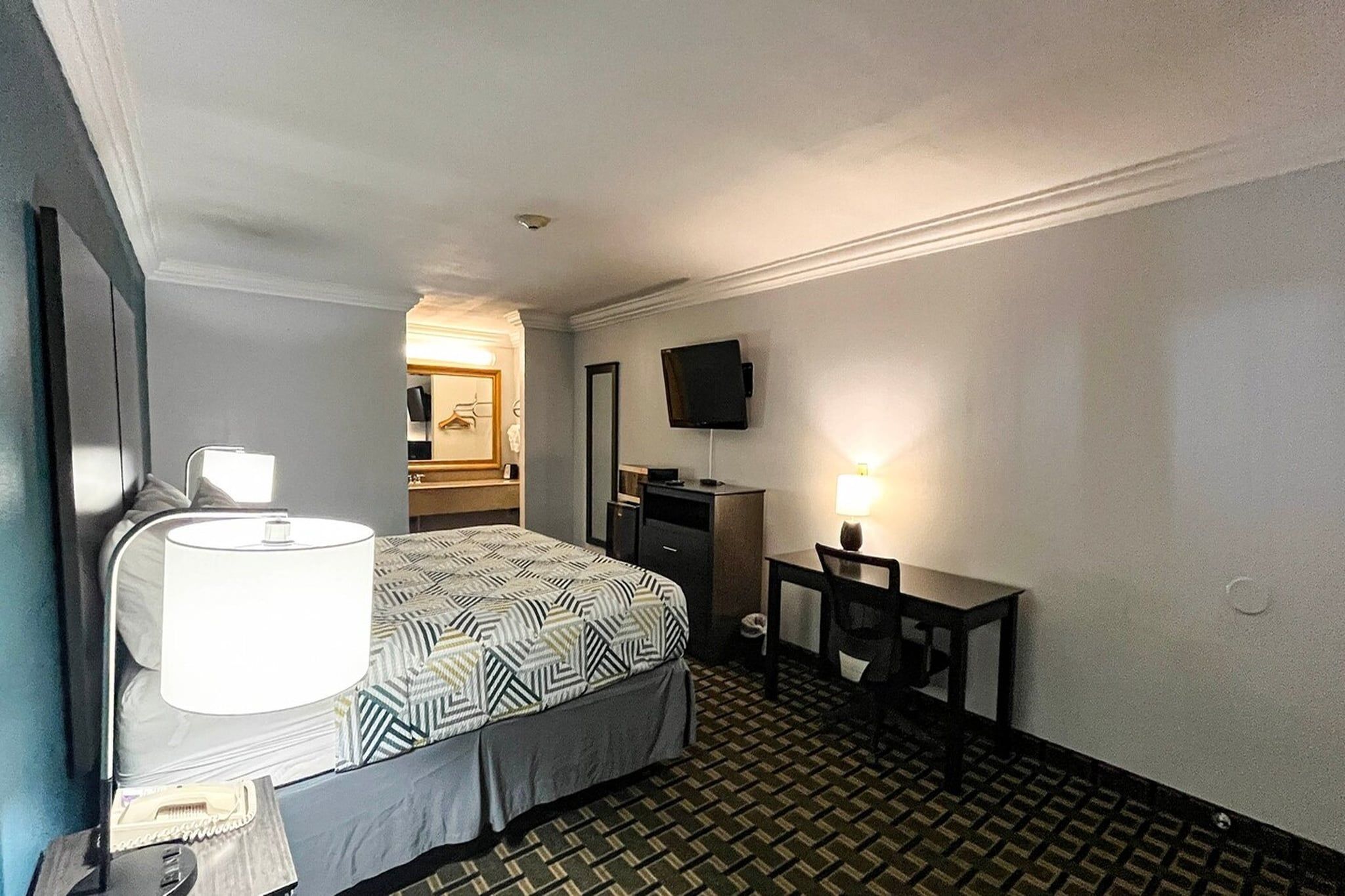 Quarto de hotel com cama, escrivaninha, televisão e banheiro visível por um arco.