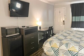 Ein Hotelzimmer mit einem Bett, einem Schreibtisch mit Lampe, einem Fernseher und einer Minibar.