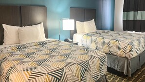 Quarto de hotel com duas camas, uma mesa de cabeceira com abajur e uma janela com cortinas.