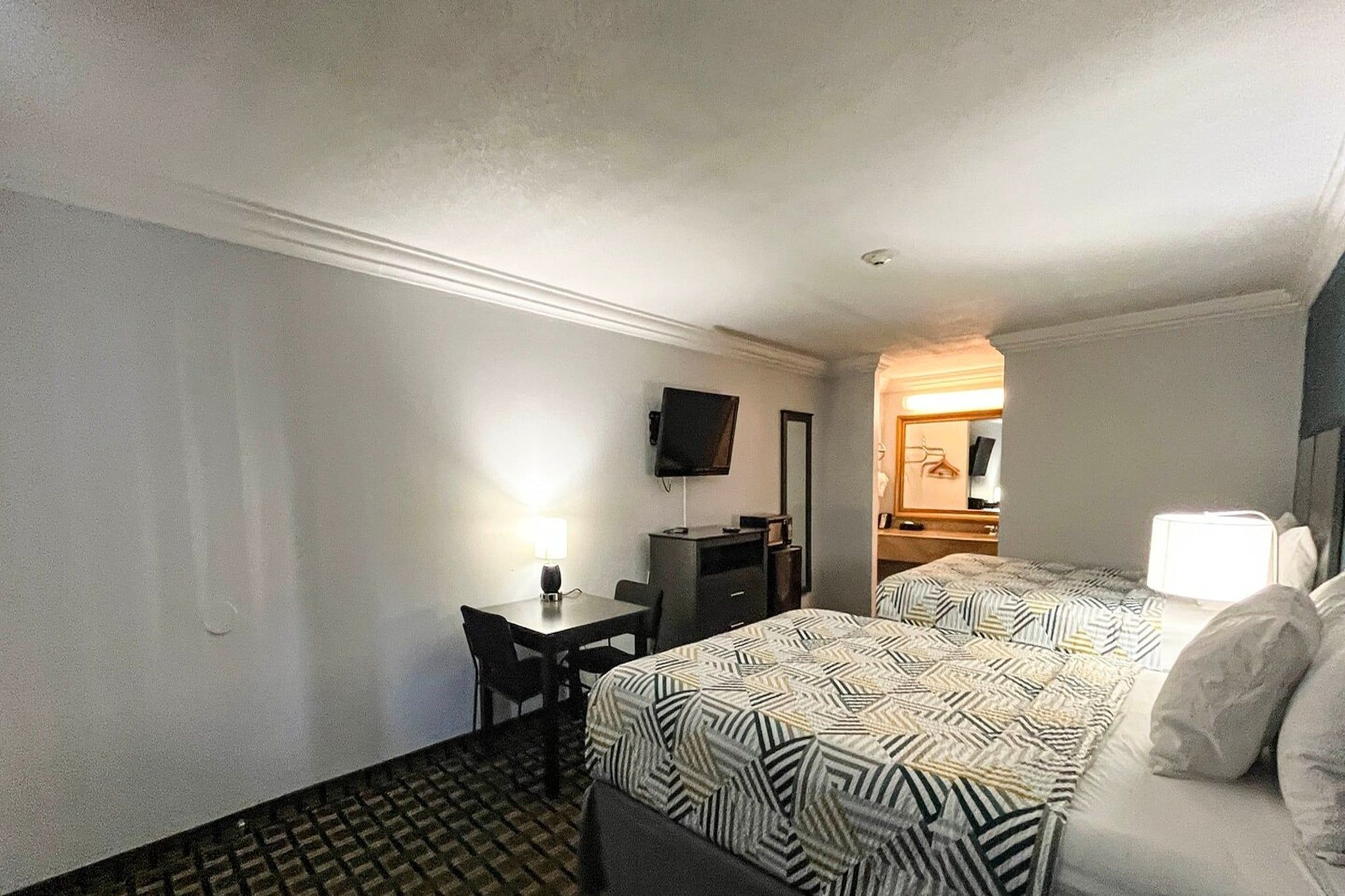 A hotel room with a bed, a desk, a chair, a television, and a mirror.