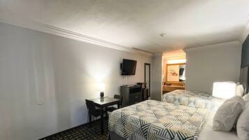 A hotel room with a bed, a desk, a chair, a television, and a mirror.