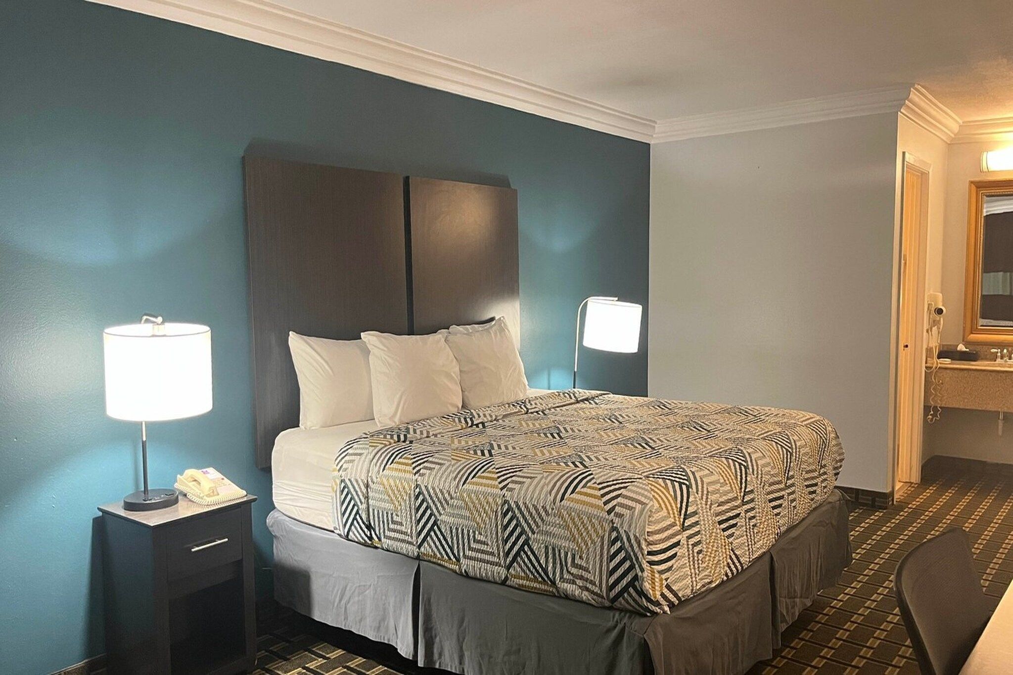 A hotel room with a bed, bedside lamps, a nightstand, and a mirror.