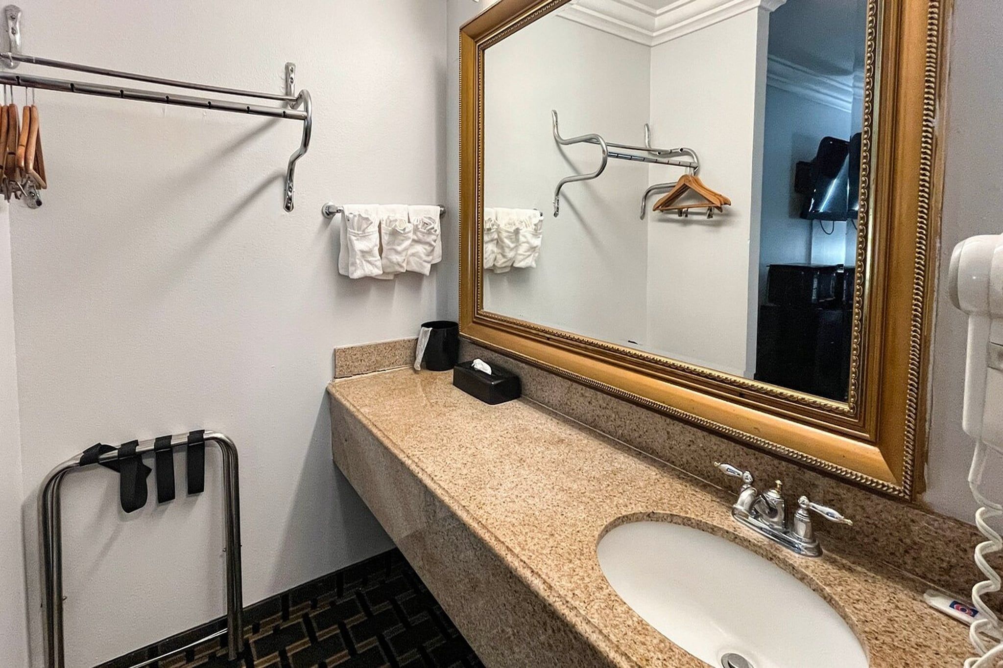 A bathroom with a sink, mirror, towel rack, and a towel dispenser.