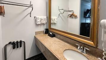 A bathroom with a sink, mirror, towel rack, and a towel dispenser.