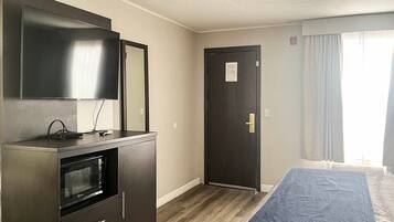 A hotel room with a bed, a television, a microwave, and a door.