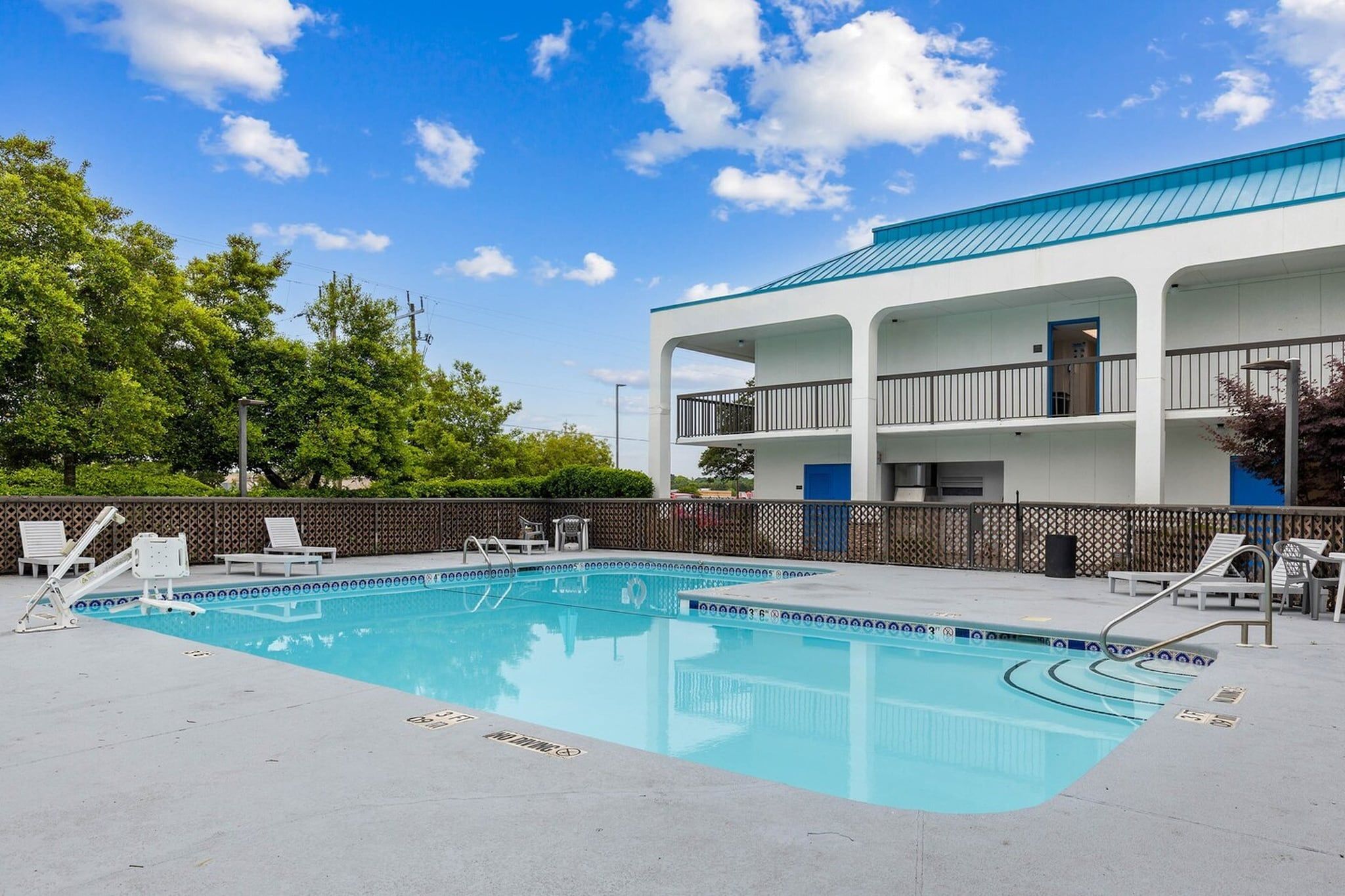 Piscina com espreguiçadeiras, área cercada e um edifício com varandas.